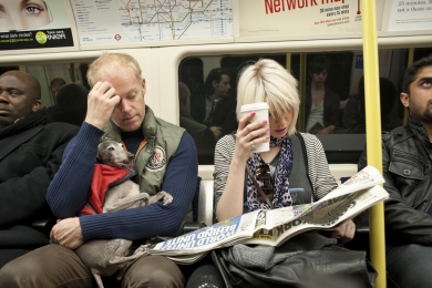 Commuters on the London underground, one man carries a old greyhound dog and a woman with pink nail varnish reads a newspaper in March 2010, England.